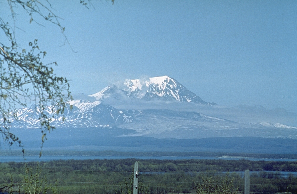 Sheveluch towers above the Kamchatka River and is one of the largest volume volcanoes in Kamchatka. A large horseshoe-shaped crater, whose northern headwall is seen in this view, formed by collapse during the Pleistocene. Repeated edifice collapse events form a vast debris avalanche plain to the south, overlain by block-and-ash flow deposits from dome collapse events. The most recent edifice collapse occurred in 1964, and the resulting deposit forms the light-colored area below the volcano to the right. Photo by Oleg Volynets (Institute of Volcanology, Petropavlovsk).