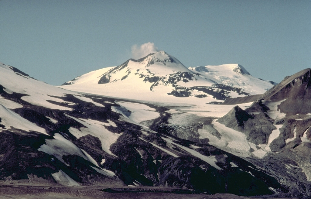 A steam plume is a nearly constant feature at the summit of Mount Martin, seen here from the NE in the Valley of Ten Thousand Smokes.  Martin volcano is extensively covered by glaciers, but is only moderately dissected.  Its youngest and largest lava flow traveled from the summit 12 km down the upper Angle Creek valley, behind the ridge at the right.  The slopes at the left are the northern flank of Mount Mageik.   Copyrighted photo by Katia and Maurice Krafft, 1978.