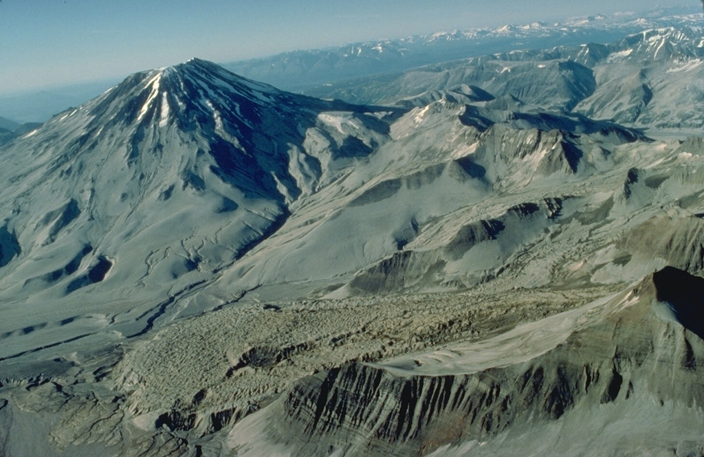 Mount Griggs is the prominent stratovolcano at the upper left in this aerial view from the SW.  The slopes of the volcano are heavily mantled with ash from the 1912 eruption of Novarupta volcano.  The 1912 pyroclastic-fall deposits also mantle the irregular surface of Knife Creek Glacier, which flows from right to left behind the ridge in the lower right foreground. Copyrighted photo by Katia and Maurice Krafft, 1978.