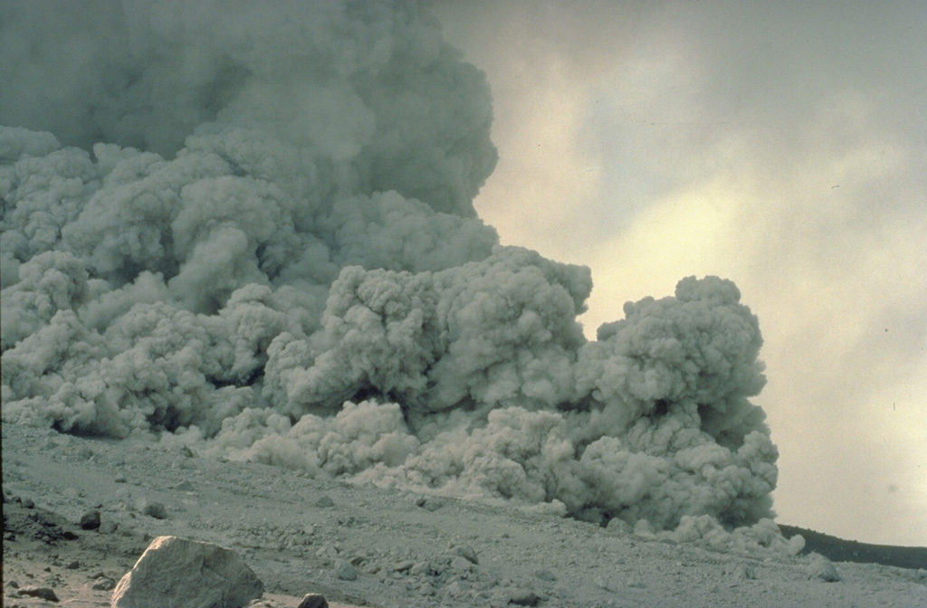 A pyroclastic flow produced by collapse of a growing lava dome sweeps down the flanks of Alaska's Augustine volcano on August 28, 1986.  These high-temperature, high-velocity flows commonly travel silently because the sound of the moving blocks at the base of the flow is muffled by dense columns of gas and ash that roil up above the flow.  This photo was taken at a distance of about 100 m from the margin of the pyroclastic flow. Copyrighted photo by Katia and Maurice Krafft, 1986.