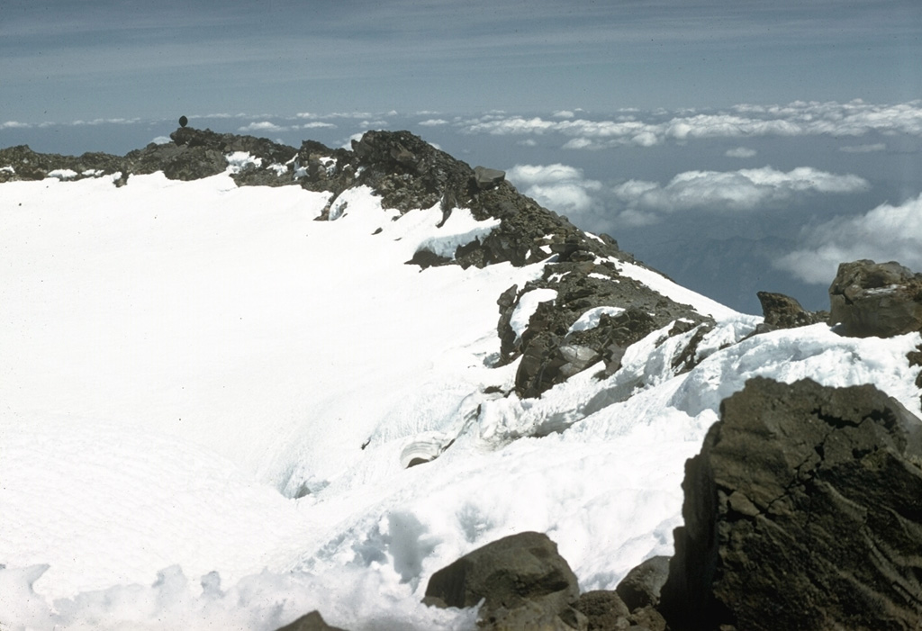 Two overlapping craters are at the summit of Mount Rainier. Continued high heat flux has produced fumaroles that have formed ice tunnels in the 100-m-deep icecap filling the eastern summit crater, shown in this 1958 photo. Ice caves are also present in the smaller western crater, which contains a small crater lake beneath the ice. Photo by Richard Fiske, 1958 (Smithsonian Institution).
