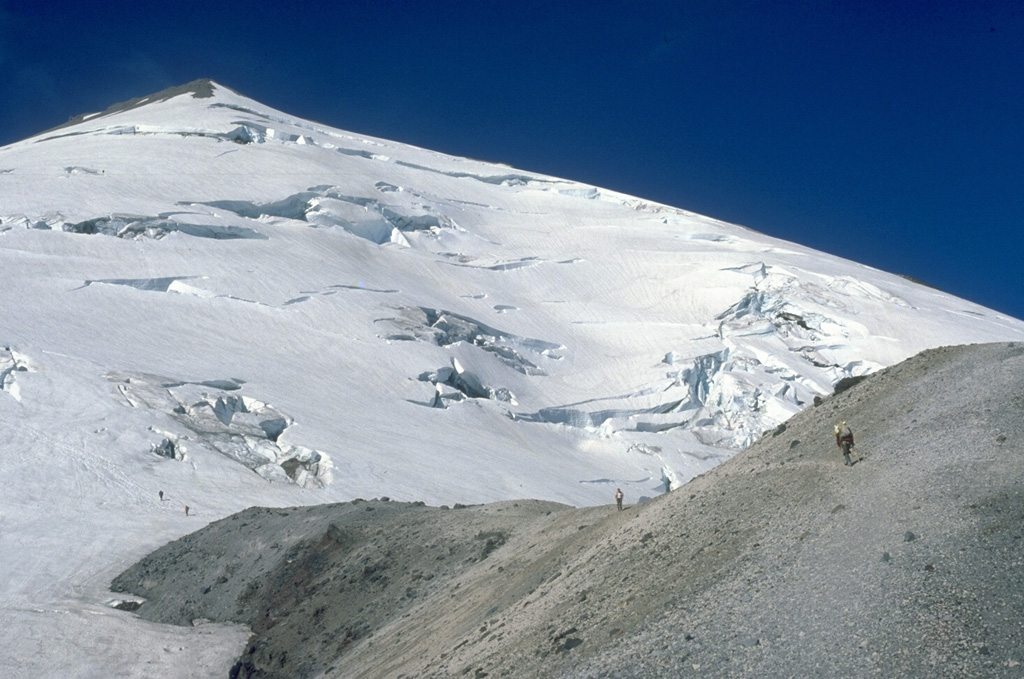 Climbers in 1979 traverse from the top of Dogs Head lava dome on the N flank onto crevassed Forsyth Glacier, with the False Summit of Mount St. Helens to the upper left. The 1980 landslide removed the summit of the volcano. Photo by Lee Siebert, 1979 (Smithsonian Institution).