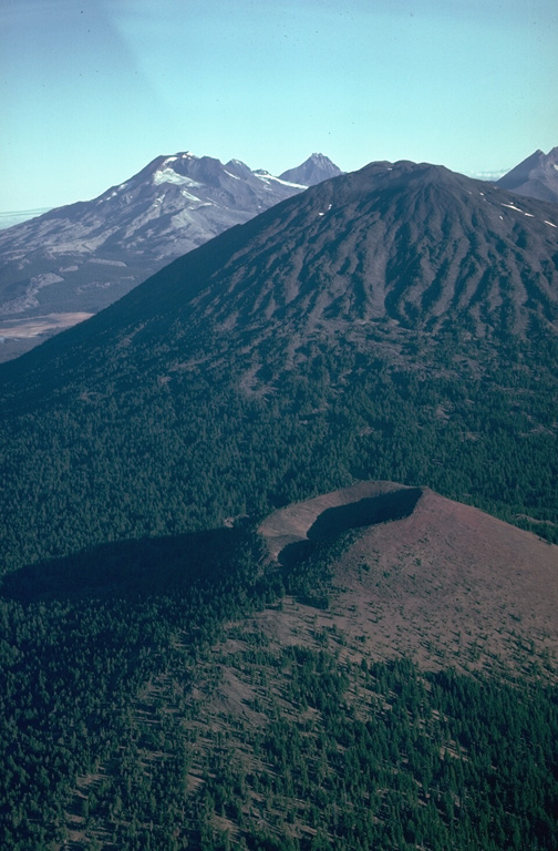 Kwohl Butte scoria cone in the foreground is part of a 25-km-long chain of small shield volcanoes and scoria cones extending north to Mount Bachelor. South and Middle Sister volcanoes are visible to the left behind the eroded slopes of Bachelor. Photo by Lee Siebert, 1981 (Smithsonian Institution).