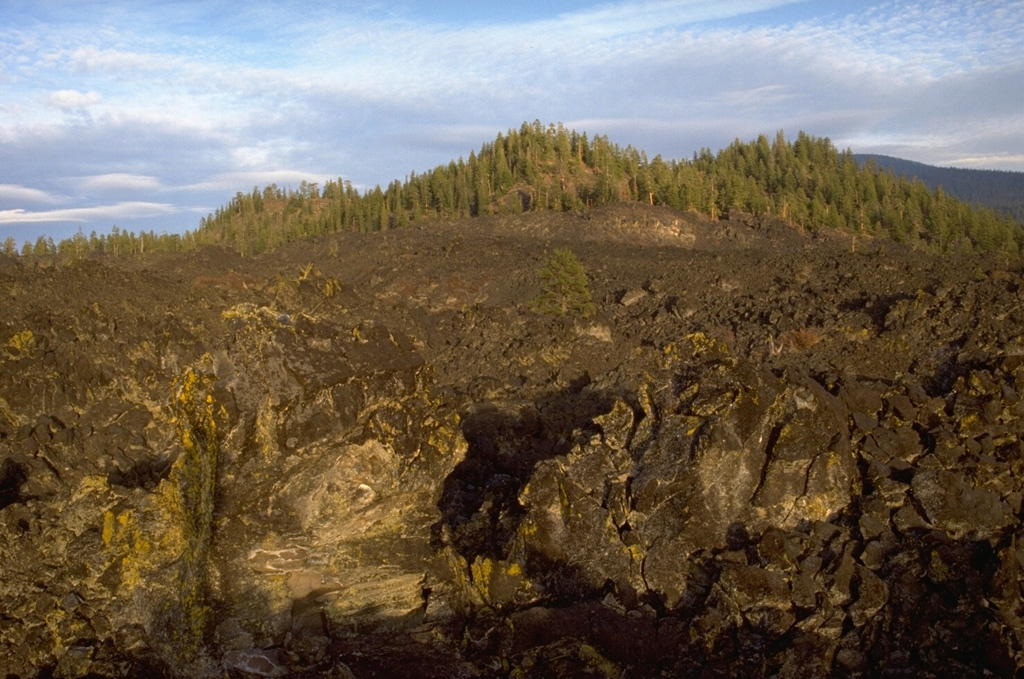 The northernmost of the three Davis Lake lava flows, each associated with a scoria cone, originated from the forested cone in the background. The lava flow spread across a broad area, creating a natural barrier that formed Davis Lake about 5,050-5,600 years ago. Photo by Lee Siebert, 1995 (Smithsonian Institution).