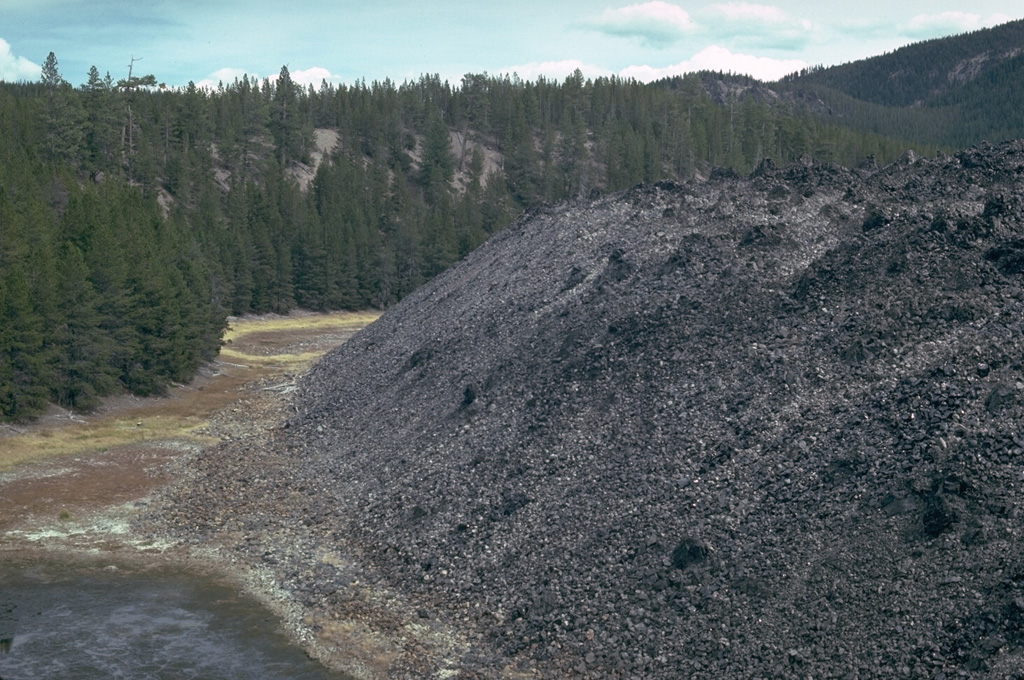 This is the NE margin of the Big Obsidian Flow, which erupted from a vent near the Newberry southern caldera wall about 1,300 years ago into this crater, whose forested rim is seen in the background.  Photo by Lee Siebert, 1981 (Smithsonian Institution).