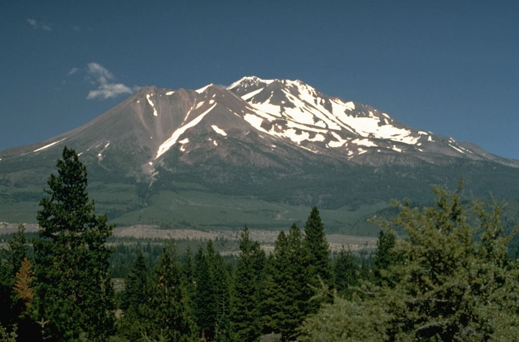 Shastina forms the largely snow-free ridge to the left of the summit of Shasta. During the growth of Shastina in the early Holocene, andesite lava flows traveled out to 14 km and pyroclastic flows swept down its flanks, covering much of the areas that are now the sites of the towns of Weed and Mt. Shasta. Photo by Lyn Topinka, 1984 (U.S. Geological Survey).