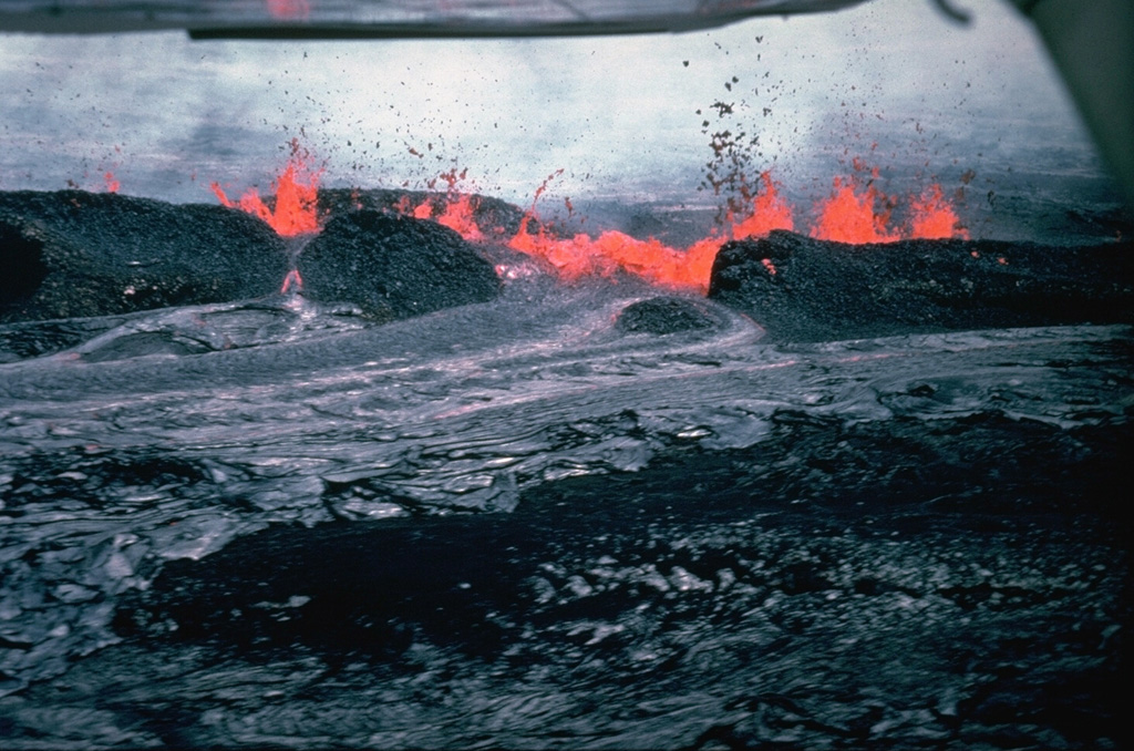 A 19-hour eruption of Kilauea began on 30 April 1982, from fissures east of Halema’uma’u crater. This view from the north shows lava spatter feeding a lava flow two hours after the start of the eruption. Spatter ramparts of the 1964 eruption are partly buried by 1982 spatter. Photo by Jack Lockwood, 1982 (U.S. Geological Survey).