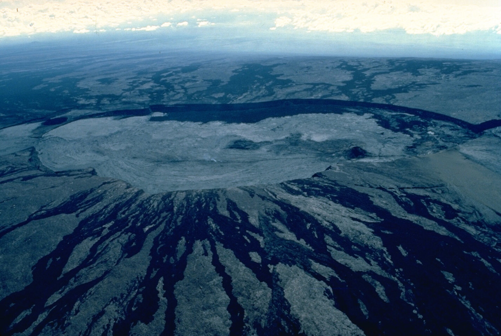 This aerial view of the summit of Mauna Loa from the NW shows the elongated, 2.4 x 4.8 km Mokuaweoweo caldera.  The walls of the flat-bottomed caldera are 80-180 m high.  Black lava flows visible on the flanks of the caldera were truncated when the caldera collapsed.  Virtually the entire caldera floor in this April 1984 view is covered with light-colored lava flows produced during the first day of an eruption in March and April of that year.  The cinder cone on the south (right) side of the caldera floor was formed during the 1940 eruption. Copyrighted photo by Katia and Maurice Krafft, 1984.