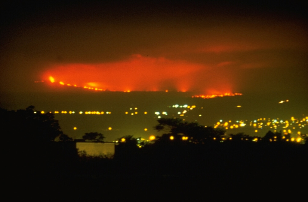 This nighttime view from the city of Hilo shows lava flows from Mauna Loa descending its NE flank on 4 April 1984. The flows traveled 42 km from vents on the upper NE rift zone of Mauna Loa, finally stopping only 5 km from the Hilo city limits. The 1984 lava flows were among the longest during historical time from Mauna Loa, matching the length of the 1942 flows. The 1855 and 1881 lava flows traveled significantly further, with the latter reaching within 2 km of Hilo Bay.  Photo by David Little, 1984 (U.S. Geological Survey).