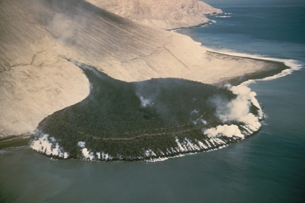 A steaming lava flow issuing from a fissure on the SE flank of Bárcena volcano, in the Revillagigedo Islands west of México, forms a peninsula about 300 m wide that extends about 230 m out to sea. This photo from the SE on 11 December 1952 was taken three days after the beginning of lava extrusion. By the time the eruption ended in February 1953 the lava delta had extended the shoreline by 700 m. Photo by Adrian Richards, 1952 (U.S. Navy Hydrographic Office).