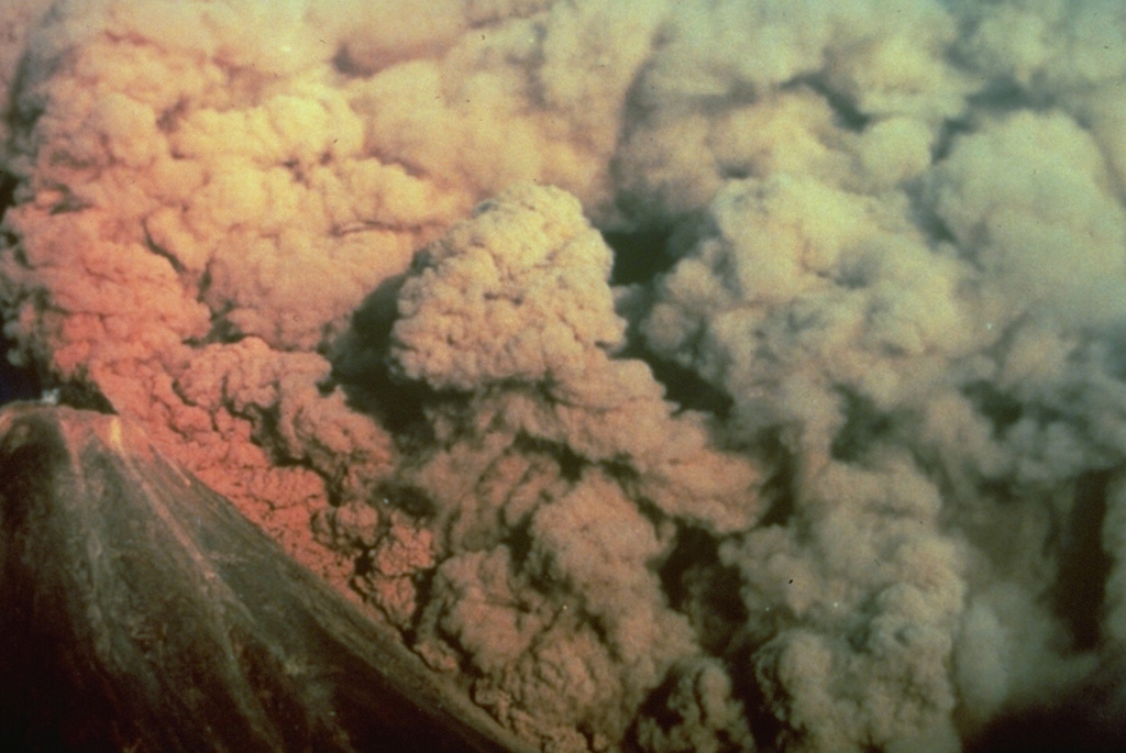 A convecting ash column rises above a small pyroclastic flow on the SW flank of Colima volcano in México on 16 April 1991. The pyroclastic flow, colored by the late-afternoon sun, was produced by the collapse of portions of the summit lava dome.  Photo by Alfredo Ramirez (pilot Ernesto Gómez Hofman), 1991 (courtesy Melchor Urzua, Protección Civil de Colima).