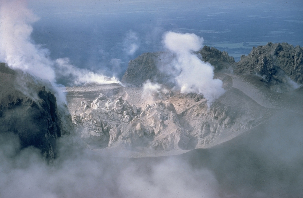 A lava dome fills Caliente crater at the eastern end of the Santiaguito dome complex in June 1968. Gases rise from fumaroles along the margins of the roughly 100-m-wide crater in this view from the north. Periodic ash eruptions accompanied growth of the dome. The Caliente vent is in the oldest part of the Santiaguito dome complex, which began erupting in 1922. It was the source of a major explosive eruption in 1929 that produced large pyroclastic flows. Photo by Dick Stoiber, 1968 (Dartmouth College).