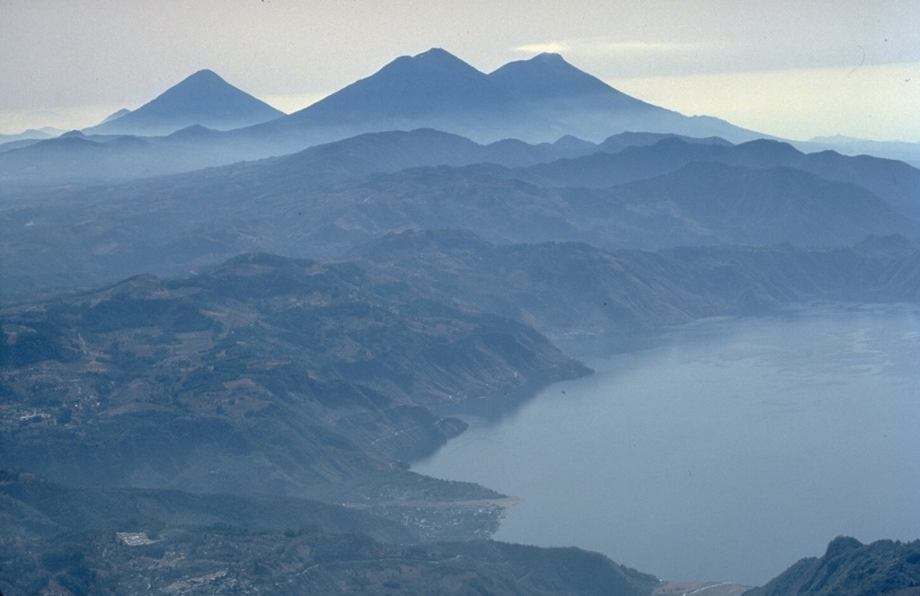 The twin volcanoes of Acatenango (left) and Fuego rise in the center beyond Lake Atitlán, with the conical peak of Agua volcano to their left.  Lake Atitlán fills the latest of three large calderas produced during the Pleistocene at Atitlán.  A steam plume originates from the summit of Fuego, one of Guatemala's most active volcanoes.  Copyrighted photo by Katia and Maurice Krafft, 1983.