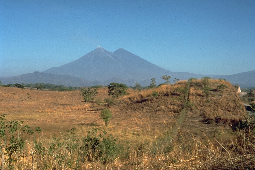 The hummocky surface in the foreground in front of the Fuego and Acatenango volcanoes in Guatemala is a massive debris-avalanche deposit in Escuintla that was produced by partial collapse of the volcanic complex sometime during the late Pleistocene to early Holocene. This is the largest known debris avalanche in Guatemala; it has an estimated volume of about 15 km3 and traveled about 50 km. For the last 30 km, the avalanche traveled over flat slopes of less than 1 degree, illustrating the extremely high mobility of volcanic debris avalanches. Photo by Jim Vallance, 1989 (Michigan Technological University).