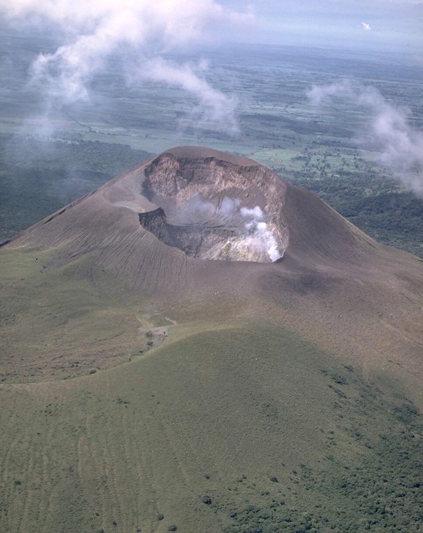 Telica, one of Nicaragua's most active volcanoes, has erupted frequently since the time of the Spanish conquest.  The Telica volcano group consists of several interlocking cones and vents with a general NW alignment.  Telica itself, seen here in an aerial view from the NE, is a steep-sided cone with a 700-m-wide double crater.  The steaming NE crater, the source of recent eruptions, is 120 m deep.  The rim of an older crater of the Telica complex forms the ridge at the lower left.    Photo by Robert Citron, 1968 (Smithsonian Institution).