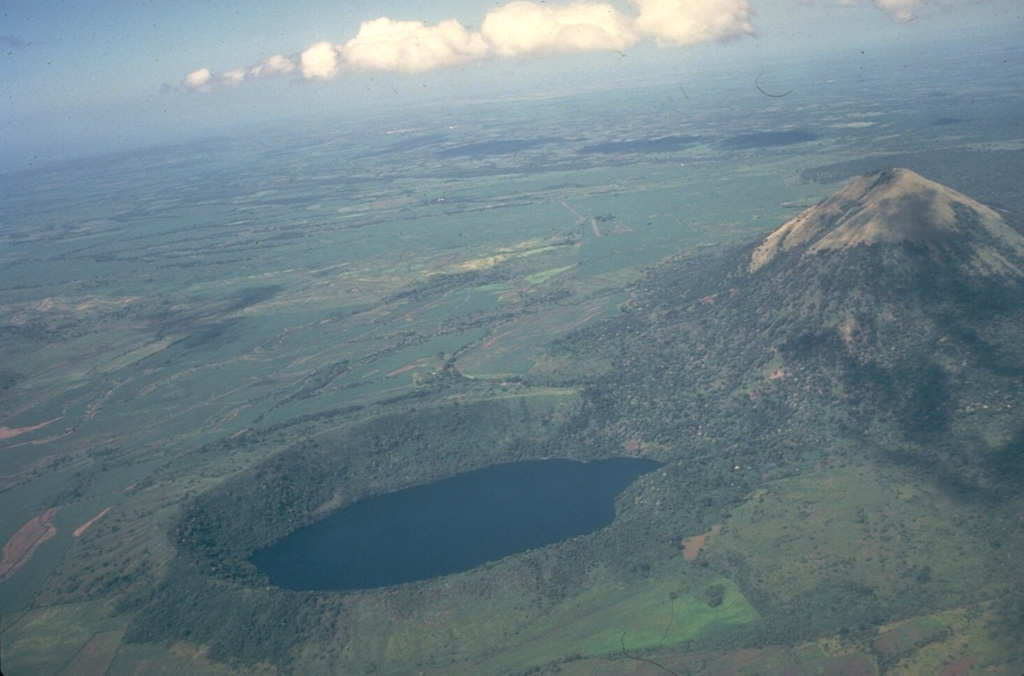 The lake-filled Laguna de Asososca maar in the foreground and the Cerro Asososca cone to the right were formed by eruptions at the southern end of a N-S fissure system of the Las Pilas volcanic complex in Nicaragua. The ages of these vents are not known. This view looks from the NE across the broad plain at the foot of the Cordillera de los Maribios to the Pacific Ocean in the distance. Photo by Jaime Incer, 1981.