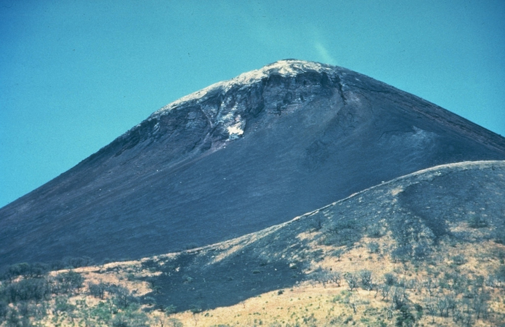 Light-colored fumarolic sublimates drape the 1297-m-high summit of Momotombo volcano, which displays strong fumarolic activity.  Fumarolic temperatures (850 degrees C) and seismicity at the volcano increased following construction of the Momotombo geothermal plant. Photo by Jaime Incer.