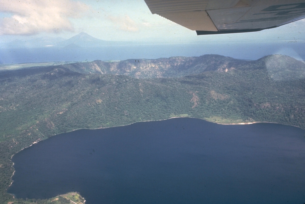Apoyeque stratovolcano forms the large Chiltepe Peninsula in central Lake Managua.  A 2.8-km wide, 500-m-deep caldera truncates the volcano's summit, below and to the left of the airplane wing.  Laguna de Jiloa, the large lake in the foreground, lies immediately SE of Apoyeque.  The age of the latest eruption of Apoyeque is not known, but human footprints underlie pumice deposits thought to originate from Apoyeque volcano or a nearby vent beneath Lake Managua.  Momotombo volcano is visible in the distance to the NW across Lake Managua.       Photo by Jaime Incer, 1981.