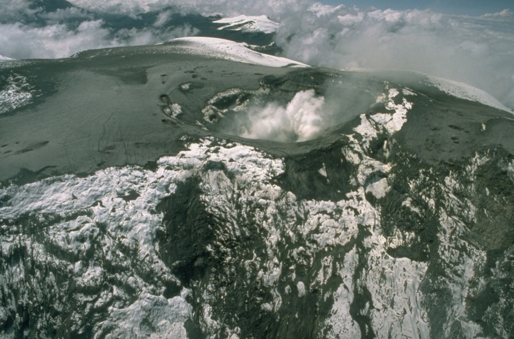A plume rises from the summit crater of Nevado del Ruiz volcano on 10 December 1985. Pyroclastic surge and ashfall deposits from the 13 November eruption coat the glaciers. Glaciers on the upper NE-flank headwall of the Azufrado valley (foreground) were scoured by pyroclastic surges. Photo by Tom Pierson, 1985 (U.S. Geological Survey).