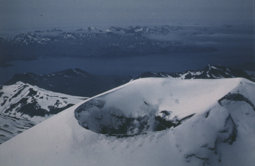 This view from the NE in June 1986 shows steam rising from the summit crater of Korovin, north of Atka. It has been reported to have a cylindrical vent of greatly variable depth depending on the presence of a lake. Photo by Harold Wilson (Peninsula Airways), 1986 (courtesy of John Reeder, Alaska Div. Geology & Geophysical Surveys).