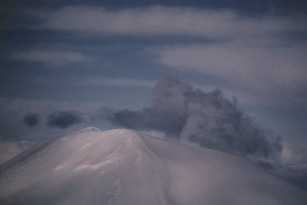 A gas-and-steam plume, possibly containing minor amounts of ash, rises above the summit of Korovin volcano on 4 March 1987. This view of Korovin, north of Atka, was taken from the south. A satellite image on 18 March showed three distinct plumes originating from Korovin and two vents to the south.  Photo by Harold Wilson (Peninsula Airways), 1987 (courtesy of John Reeder, Alaska Div. Geology Geophysical Surveys).