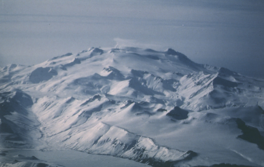Makushin is a glaciated volcano on northern Unalaska Island. This 2 March 1987 view from the NE shows a small plume originating from a vent on the left side of the broad summit and drifting about 3 km WNW. The summit contains a 2-km-wide caldera. Minor explosive eruptions have occurred during historical time. Photo by Harold Wilson (Peninsula Airways), 1987 (courtesy of John Reeder, Alaska Div. Geology Geophysical Surveys).