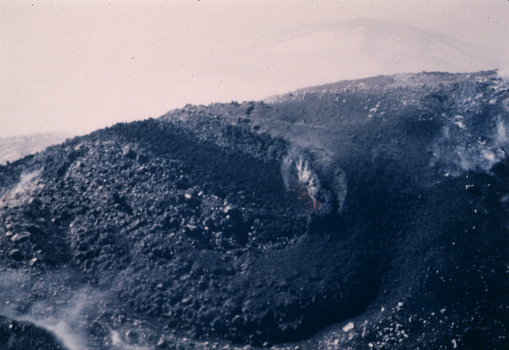 An eruption of Cleveland in 1987 began with explosive activity on 19 June that deposited ash onto snow on the flanks. On 23 June, the date of this photo, a lava flow from the summit eventually extended 2.5 km down the ESE flank. Lava fountaining was observed on 22 July, and on 28 August a large explosive eruption produced an ash plume that reached over 10 km altitude. Photo by Harold Wilson (Peninsula Airways), 1987, courtesy of John Reeder (Alaska Div. Geology & Geophysical Surveys).