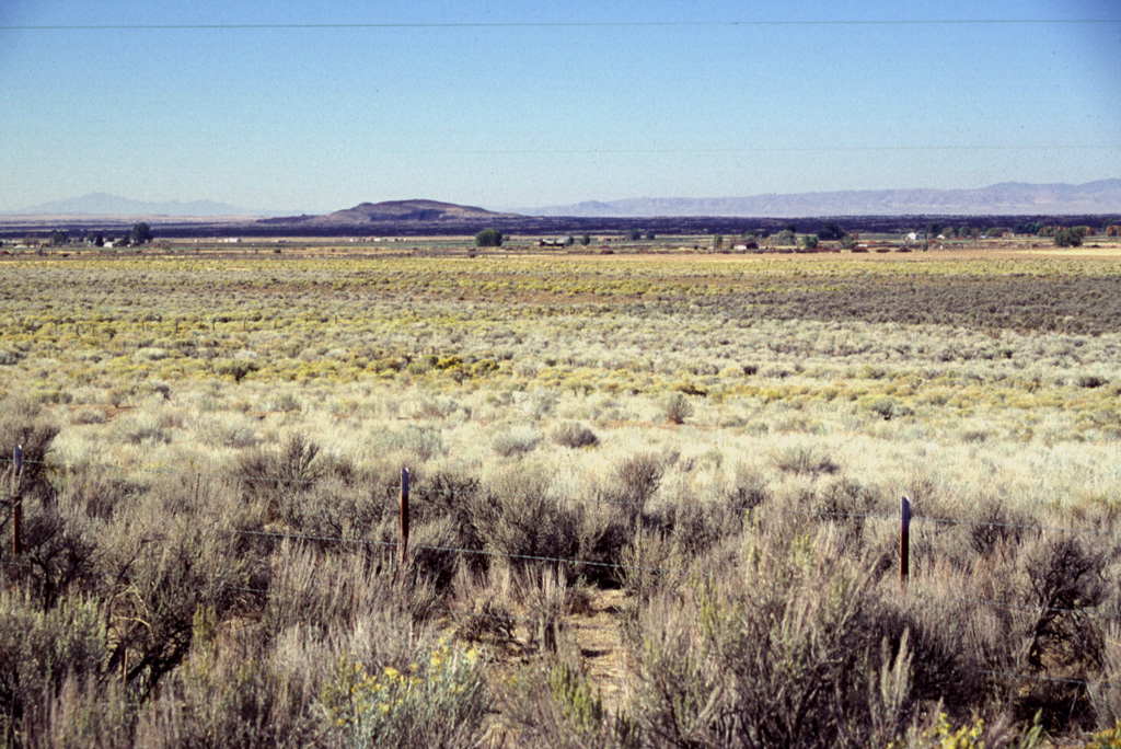 The inconspicuous hill on the left-center horizon to the SW is Ice Springs volcano, part of the Black Rock Desert volcanic field in central Utah.  The black area extending across the photo from the cinder cone complex is a 660-year-old basaltic lava flow from Ice Springs volcano.  An additional NNE-SSW chain of small volcanic vents is located NE of the main vent complex.  The volcanic fields in the Black Rock Desert area were first described by pioneering U.S. Geological Survey geologist G.K. Gilbert in the late 19th century. Photo by Lee Siebert, 1996 (Smithsonian Institution).