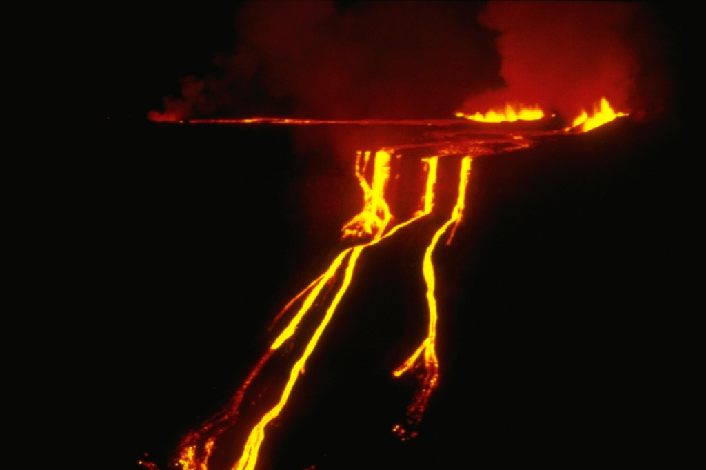 A fissure eruption on the SE caldera bench of Fernandina volcano feeds lava flows that form a spectacular, 530-m-high cascade of molten lava down the caldera wall.  A four-day-long eruption began on March 23, 1977 from fissures on the west side of the SE caldera bench, 300 m below the caldera rim.  Lava flows can be seen spreading out over the caldera bench before pouring over the caldera wall.  The distal end of the lava flows formed a small lava delta in the 2-km-wide caldera lake.   Photo by Dagmar Werner, Charles Darwin Research Station, 1977 (courtesy of Tom Simkin, Smithsonian Institution).