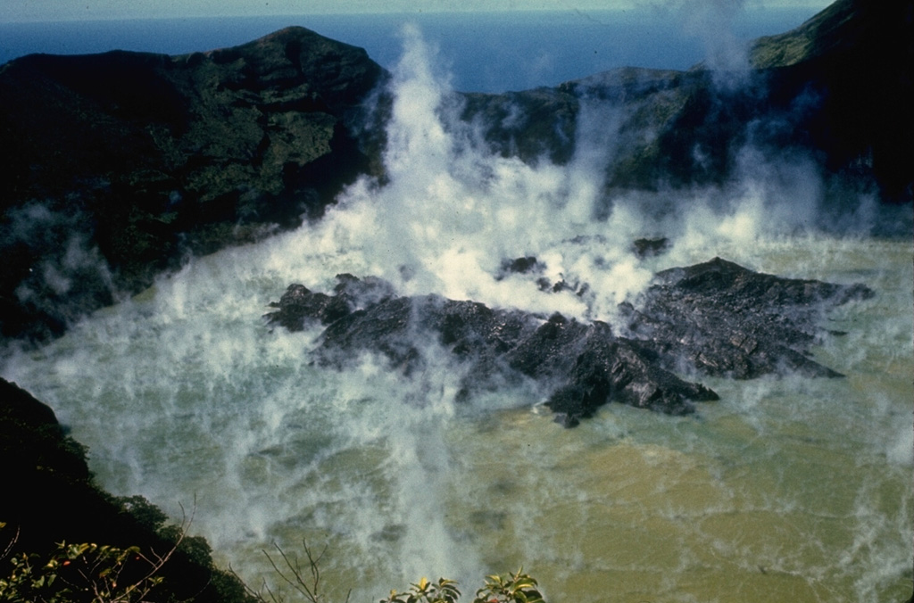 A growing lava dome rises above the surface of the steaming crater lake of Soufrière volcano in December 1971.  The dome first breached the surface of the lake on November 20, after extrusion began sometime in late September or early October.  Its height increased at an intial rate of 2-3 m/day before it stopped growing on March 20, 1972.  Unlike other historical eruptions of Soufrière St. Vincent volcano, the 1971-72 eruption was non-explosive. Photo by Jack Frost, 1971.