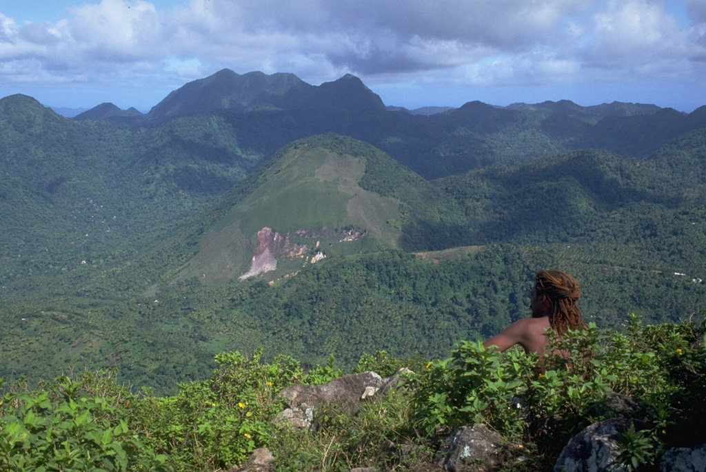 The rounded Terre Blanche lava dome (center) was constructed within the 3.5 x 5 km wide Qualibou caldera.  The dome is seen here from the summit of Petit Piton, a pre-caldera lava dome, with the skyline ridge forming the NE caldera wall.  Andesitic lava flows and breccias are exposed in the caldera wall.  The 450-m-high Terre Blanche dome is one of 3 dacitic lava domes that grew following formation of the caldera about 39,000 years ago. Photo by Lee Siebert, 1991 (Smithsonian Institution).