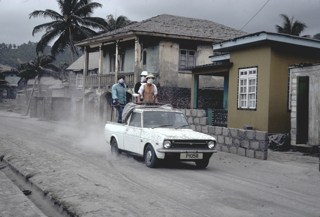 A truck filled with people evacuating the eruption of Soufrière volcano drives through the streets of the city of Georgetown, SE of the volcano, in April 1979.  The riders are wearing masks because of ashfall.  About 15,000 people were initially evacuated from the northern half of the island, which had been devastated by a previous eruption in 1902. Photo by Richard Fiske, 1979 (Smithsonian Institution).