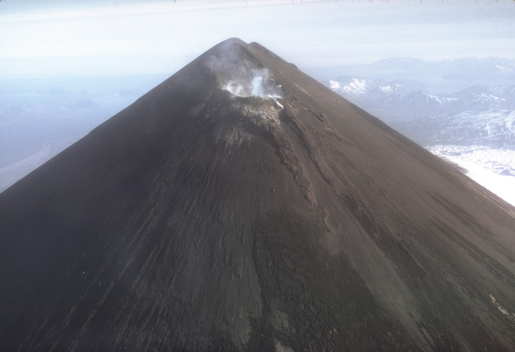 The entire upper flanks of Pavlof are darkened by ash in this November 1973 photo taken after a 12-13 November explosive eruption. Small plumes rise from the crater on the uppermost NE flank just below the normally snow-covered summit. Photo by Tom Miller, 1973 (Alaska Volcano Observatory, U.S. Geological Survey).