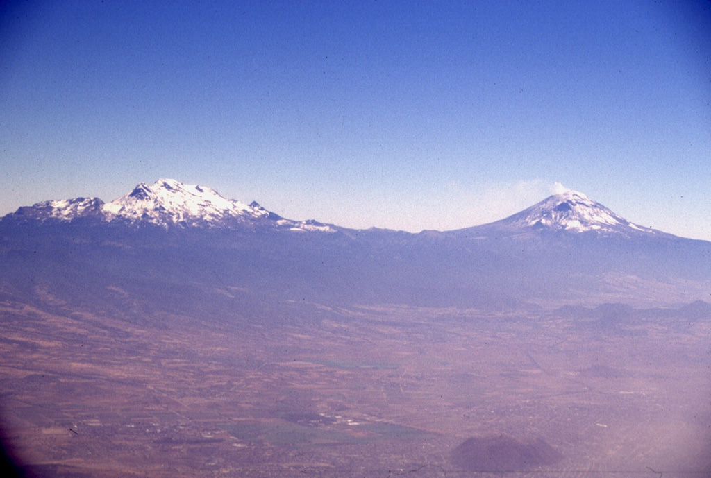 Iztaccíhuatl (left) and Popocatépetl (right) seen east of the Valley of Mexico. The differing profiles of the two volcanoes are due to varying styles and durations of volcanism. Iztaccíhuatl's elongate form reflects migration of volcanism over long periods of time along a NNW-SSE trend; it is largely Pleistocene in age, and has been extensively eroded. The more symmetrical Popocatépetl is much younger and has more-localized vents.  Photo by Lee Siebert, 1997 (Smithsonian Institution).