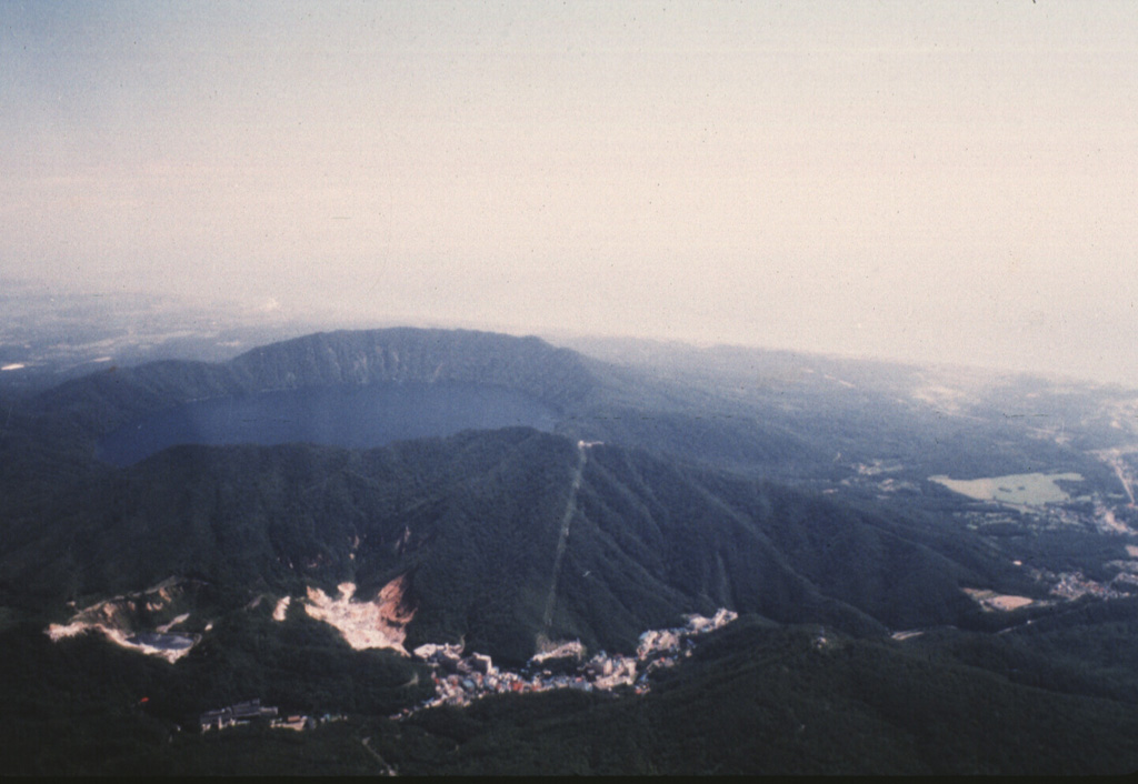 Kuttara volcano consists of a 3-km-wide, lake-filled caldera seen here from the W, near the Pacific coast of Hokkaido. Post-caldera eruptions have produced a series of explosion craters on the west flank. Thermal activity associated with these craters has produced large areas of hydrothermally altered ground seen at the bottom of the photo. The resort town of Noboribetsu Spa is visible at the lower center. Photo by Yoshio Katsui, 1996 (Hokkaido University).