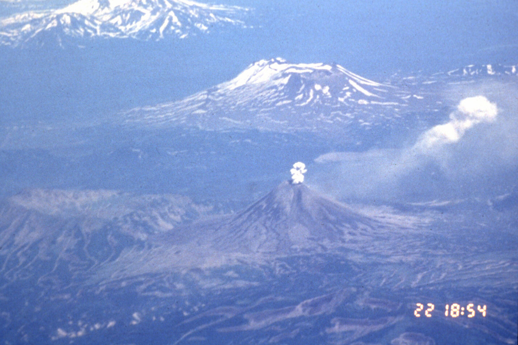 An aerial view from the SW on 22 July 1996 shows an ash plume rising above the summit crater of Karymsky with Maly Semyachik behind it. The 1996 eruption began on 2 January simultaneously with an eruption at nearby Akademia Nauk caldera, out of view to the right. The Akademia Nauk eruption lasted only a day, but long-term eruptions continued at Karymsky.  Photo by Phillip Kyle, 1996 (courtesy of Vera Ponomareva, Institute of Volcanic Geology and Geochemistry, Petropavlovsk).