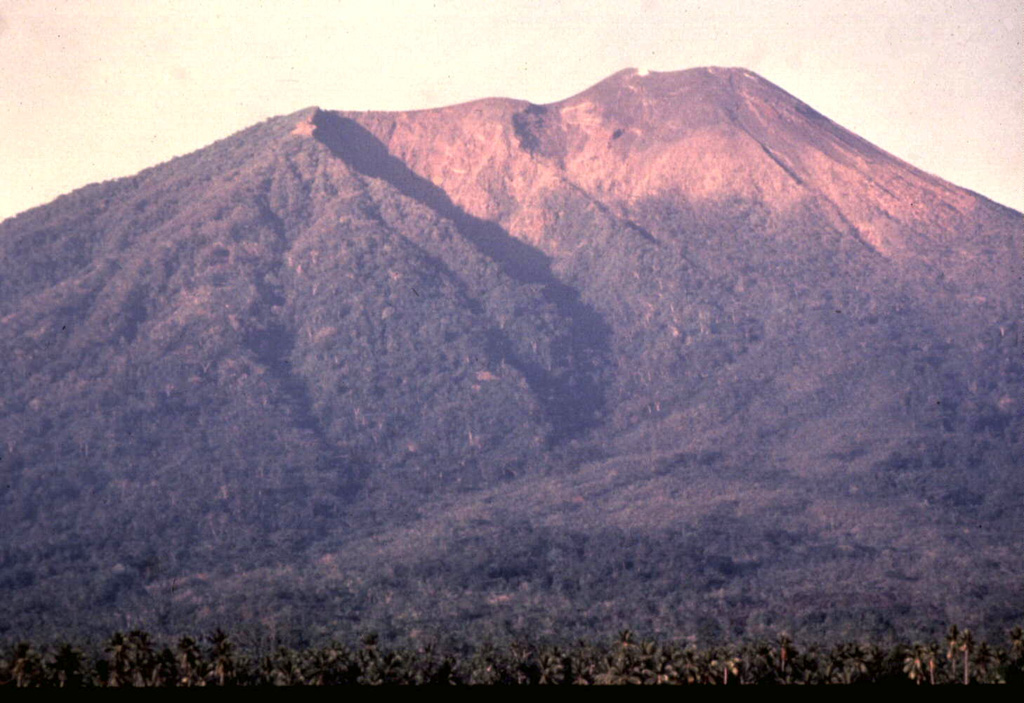 The three craters forming the summit of Gamalama volcano are visible in this view from the NE flank.  The craters have migrated to the north, with the modern cone (right) forming the present summit of the volcano.  The prominent shadow cutting diagonally to the right marks the rim of the older GI crater, inside of which the GII cone and crater grew.  The GIII crater truncates the flat-topped summit of Gamalama. Photo by Jack Lockwood, 1980 (U.S. Geological Survey).