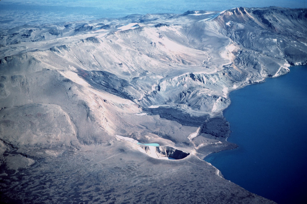 The dark 1921 Batshraun lava flow descends from a vent (left center) on the caldera rim into Öskjuvatn lake across several fault blocks related to caldera subsidence. This aerial view from the northwest shows the small 200-m-wide Viti maar (lower center), which formed during the 1875 eruption. Following slow subsidence of the caldera during and after the 1875 eruption, the depression was filled by the waters of Öskjuvatn lake. During the 1920's, several lava flows erupted from vents surrounding the caldera and flowed into the lake. Photo by Michael Ryan, 1984 (U.S. Geological Survey).