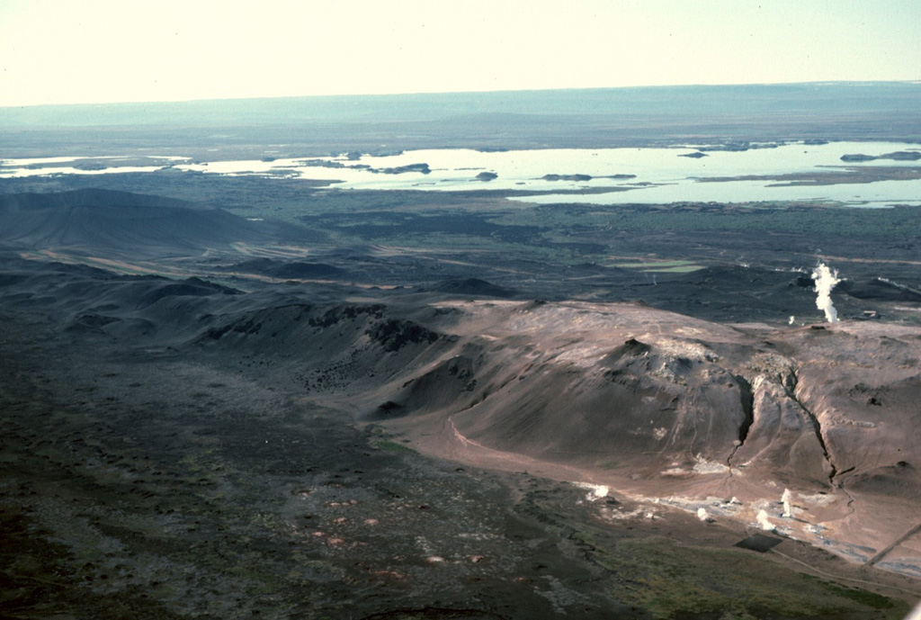 The Námafjall hyaloclastic ridge, formed as a result of subglacial eruptions, cuts diagonally across the foreground of the photo, with Mývatn lake in the middle distance to the SW. The discoloration of the ground on and around the ridge is due to the geothermal activity causing alteration in the rocks. Steam plumes can be seen both in front and behind the ridge from geothermal sites. The site in the foreground at the bottom of the ridge is Hverir, a geothermal tourist attraction. Photo by Michael Ryan, 1984 (U.S. Geological Survey).
