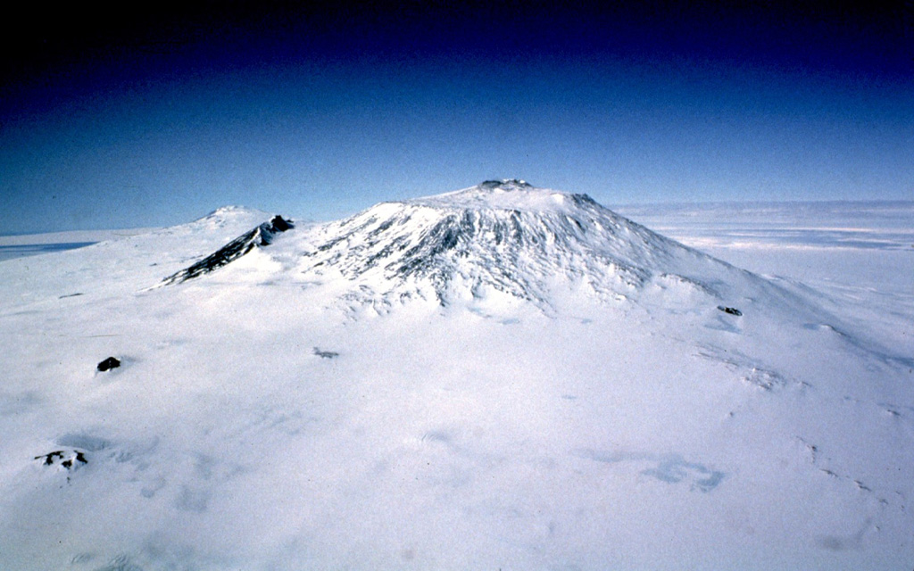 Mount Erebus is seen here from the west and is Earth's southernmost active volcano. A largely infilled caldera forms a plateau at the summit where the active cone is located. Fang Ridge is the dark area on the NE flank (left). Photo by Bill Rose, 1983 (Michigan Technological University).