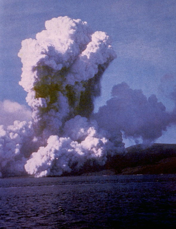 A plume of ash and steam rises above Telefon Bay on 4 December 1967. The eruption occurred from submarine vents in Telefon Bay, in the northwest part of the caldera bay, forming a new island named Yelcho. A second eruption center opened on land to the east.  During the peak of activity the plume rose over 10 km above the vent, and pyroclastic material covered most of Deception Island. Ashfall occurred throughout the South Shetland Islands. Photo by British Antarctic Survey, 1967 (published in González-Ferrán, 1995).