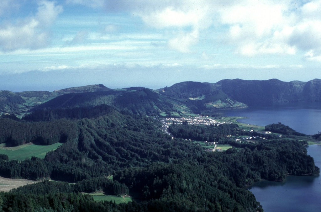 The western section of the Sete Cidades caldera is seen in this view from the southern caldera rim. Lagoa Verde (bottom right) and Lagoa Azul (center right) stretch across the center of the caldera, bounded to the east and west by pyroclastic cones. Here, three forested cones can be seen that formed during the past 5,000 years. These are the Caldeira Seca (left), Caldeira do Alferes (left center), and Seara (behind and to the right of Alferes). The broadly circular caldera forms the horizon in the background. Photo by Rick Wunderman, 1997 (Smithsonian Institution).
