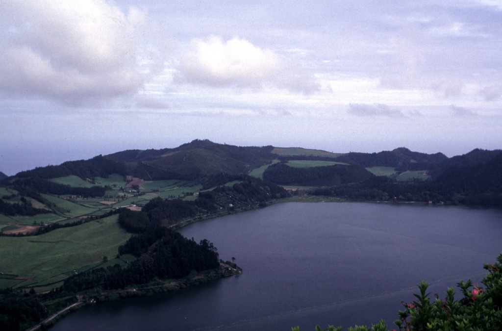 Furnas volcano, at the eastern end of Sao Miguel Island, contains two nested calderas. The southern rim of the younger 6-km-wide caldera is seen here from the north, with Furnas Lake on the right foreground. At least 10 trachytic pumice layers, all erupted during the past 5,000 years, post-date the caldera. The dome with the semi-circle of trees in the center behind the lake is the site of the most recent eruption at Furnas, a sub-Plinian eruption in 1630 CE. Photo by Rick Wunderman, 1997 (Smithsonian Institution).