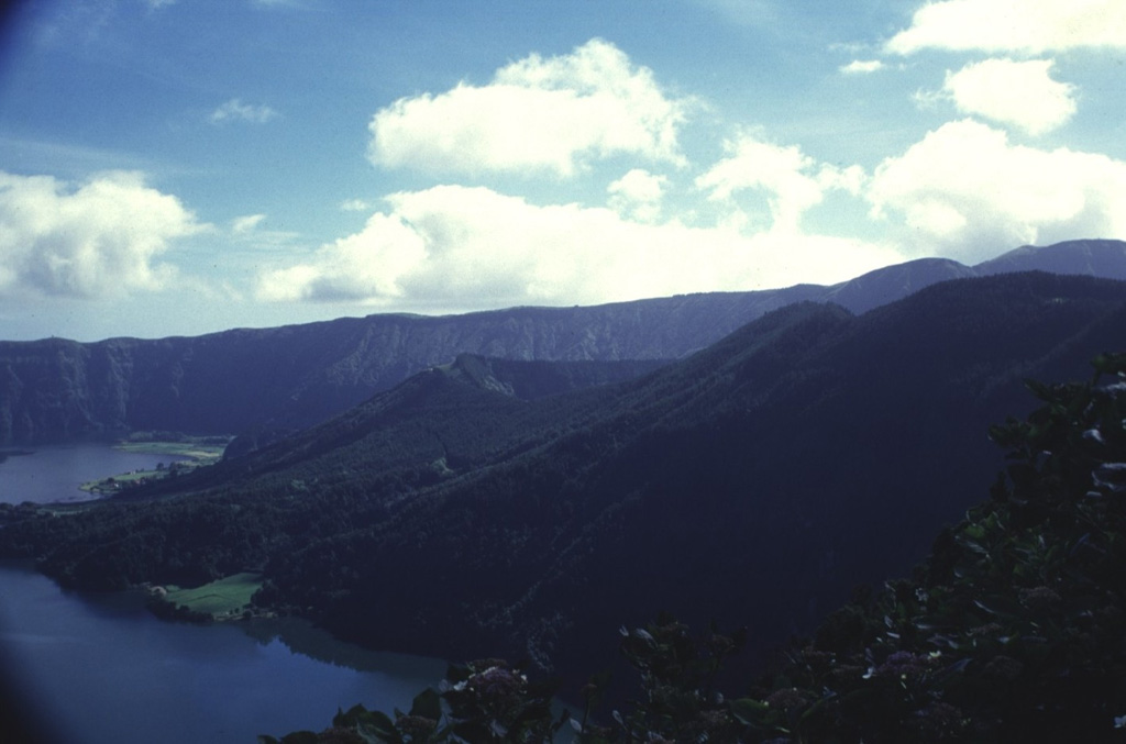 The SE floor of Sete Cidades caldera contains a large trachytic lava dome with two craters containing Lagoa de Santiago and Lagoa Rasa. The rim of Lagoa de Santiago crater is visible in the center. The visible lakes in this image are the Lagoa Verde (left foreground) and Lagoa Azul (left background), that occupy much of the caldera floor. Both explosive eruptions forming Santiago and Rasa occurred within the last 5,000 years. Photo by Rick Wunderman, 1997 (Smithsonian Institution).