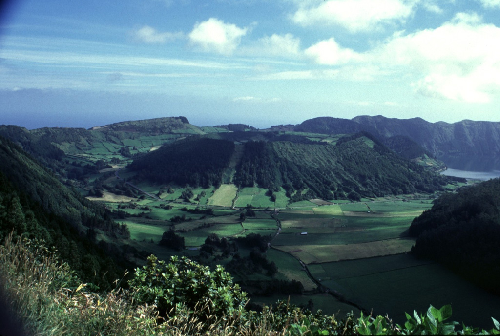 Caldeira do Alferes (center) is one of a group of pyroclastic cones constructed on the floor of Sete Cidades caldera. The adjacent cone of Seara is just visible in the background, right of Caldeira do Alferes in this view from the western caldera rim. The forested slope seen in the right foreground is Caldeira Seca. Explosive trachytic eruptions occurred at least 17 times in the past 5,000 years within the caldera.  Photo by Rick Wunderman, 1997 (Smithsonian Institution).