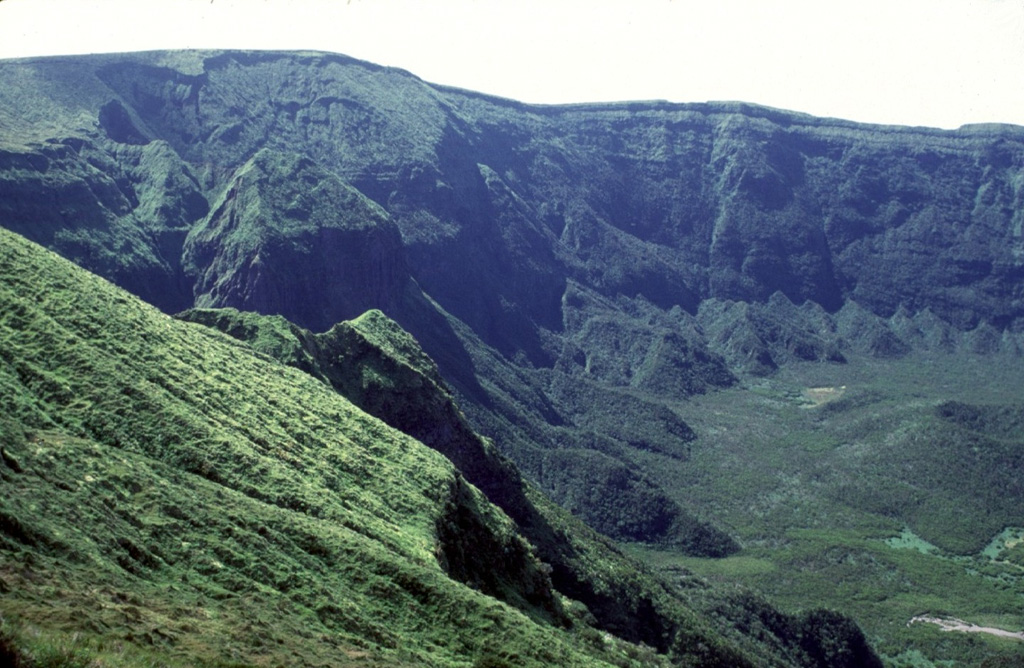 The steep vegetated northwest wall of the 2-km-wide summit caldera of Fayal volcano rises about 400 m above the caldera floor. A small pyroclastic cone is visible at the lower right. It is thought that this caldera formed in stages, beginning with a large explosive eruption about 1,000 years ago. Photo by Rick Wunderman, 1997 (Smithsonian Institution).