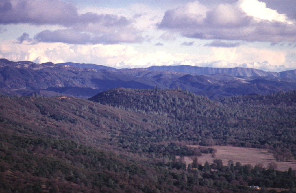 Round Mountain (center), seen here from the WNW with the hills of the California Coast Range in the background, is one of a series of basaltic-andesite cinder cones erupted along a N-S-trending line at the eastern margin of the Clear Lake volcanic field.  These cones form some of the youngest products of the volcanic field.  Lava flows from Round Mountain extend west into High Valley (lower right) and east to the North Fork Cache River.  The background hills are composed of Cretaceous-Jurrasic metamorphic rocks of the Franciscan formation. Photo by Paul Kimberly, 1997 (Smithsonian Institution).
