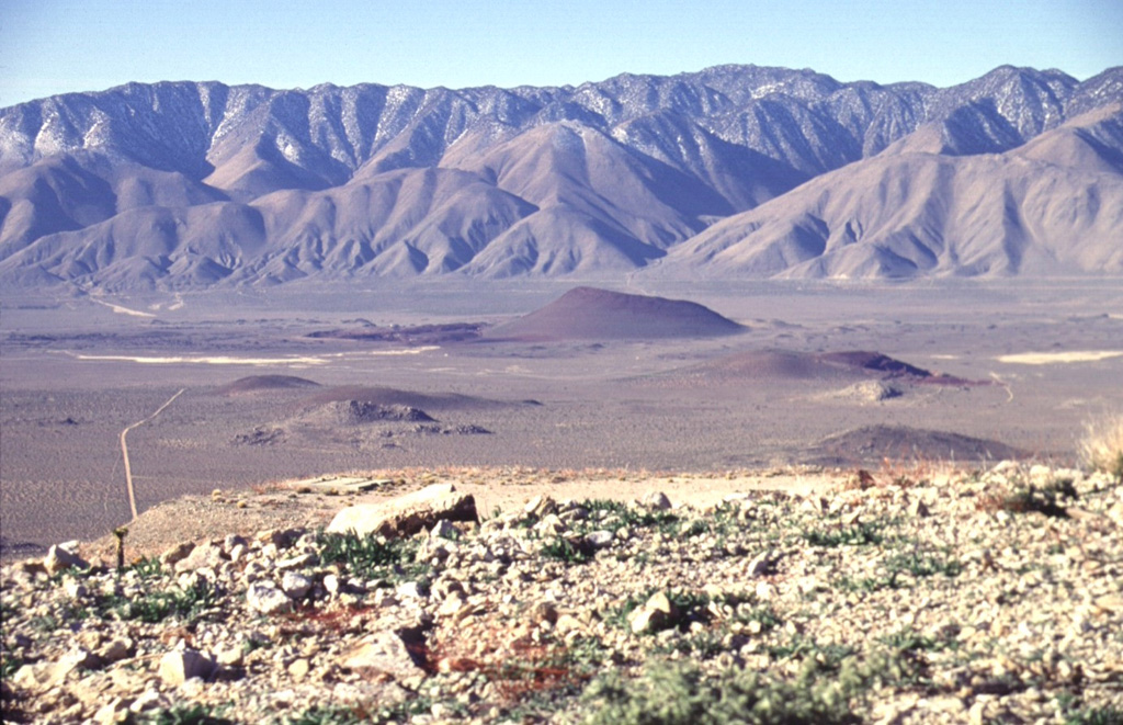 Red Cone (center) is the largest of a group of isolated basaltic scoria cones and lava flows on the floor of the Rose Valley in the western part of the Coso volcanic field.  The late-Pleistocene scoria cone is seen here from the NE, with the towering fault scarp of the Sierra Nevada Range in the background.  Highway 395 traverses Rose Valley between the cone and the Sierras.    Photo by Lee Siebert, 1997 (Smithsonian Institution).