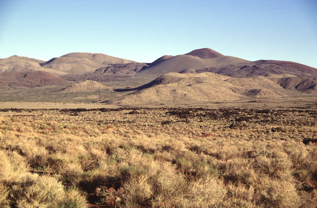 A series of basaltic cinder cones and related lava flows at the southern end of the Coso volcanic field form some of the youngest volcanic products at Coso.  The cones and flows are concentrated along the south edge of a NE-trending horst that is capped by rhyolitic lava domes and flows.  Many of the flows, such as the one left of center, are intracanyon flows that traveled down existing drainages. Photo by Lee Siebert, 1997 (Smithsonian Institution).