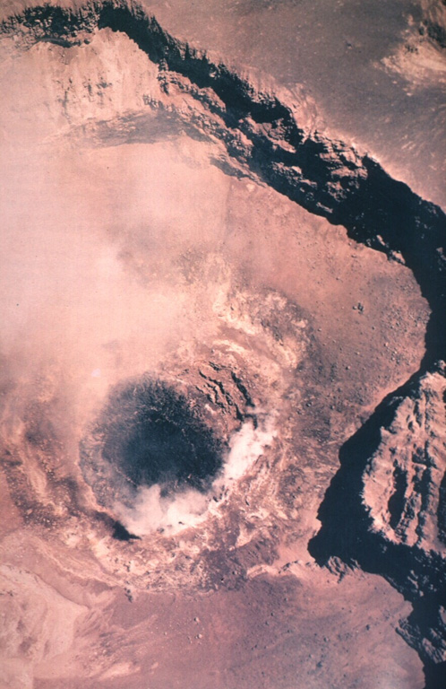 A vertical aerial view into the summit crater of Láscar shows a dark-colored dacitic lava dome that was extruded inside the active crater between February and December 1989.  Ash eruptions had begun earlier in late 1987 and had continued in 1988.  The active lava dome was observed in February and April 1989, and the dome was observed to be deflated in October 1989.   An explosive eruption on February 20, 1990 destroyed 10-30% of the summit crater lava dome and produced an 8-km-high ash cloud.   Photo by Servicio Aerofotogramétrico de la Fuerza Aérea de Chile, 1989 (courtesy of Oscar González-Ferrán, Univ Chile).